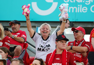 An Adelaide United supporter smiling in the grandstand holding two teddy bears