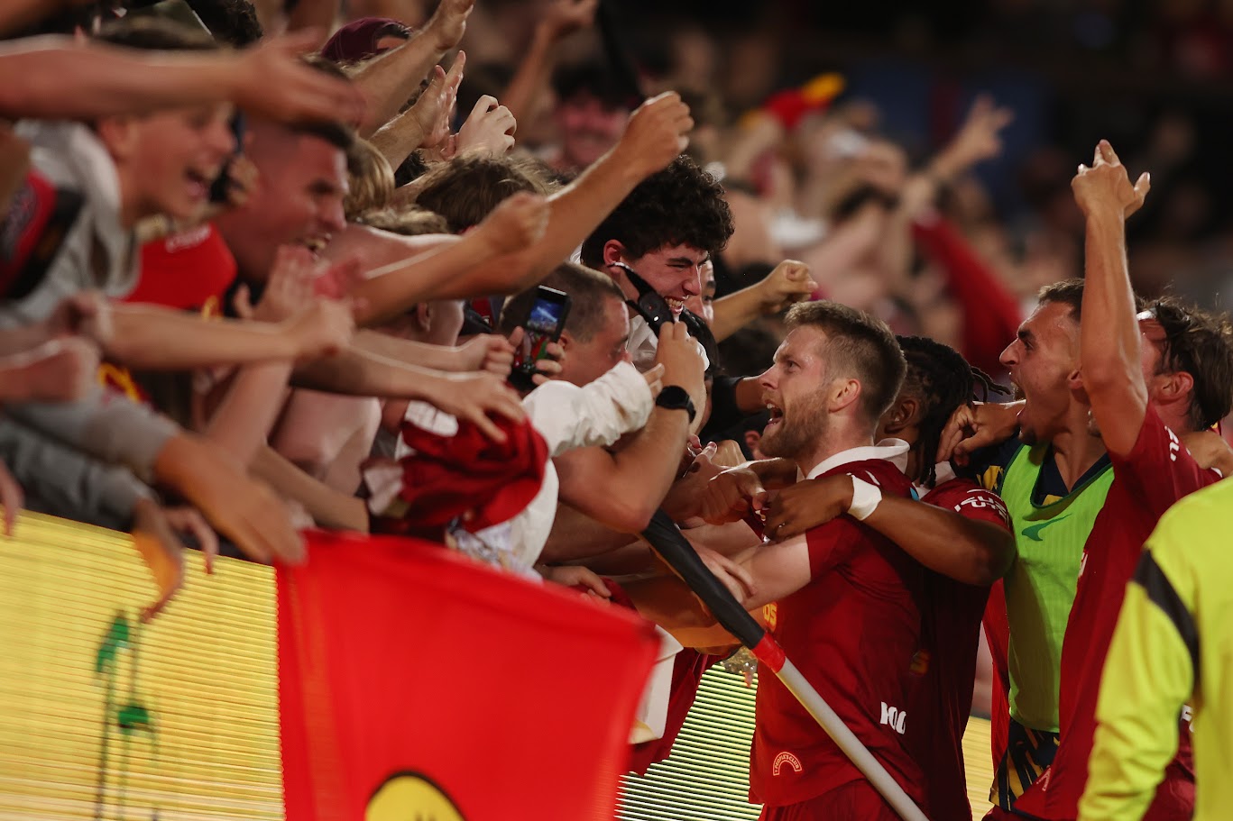 An Adelaide United player celebrating with supporters over the barrier at a night match