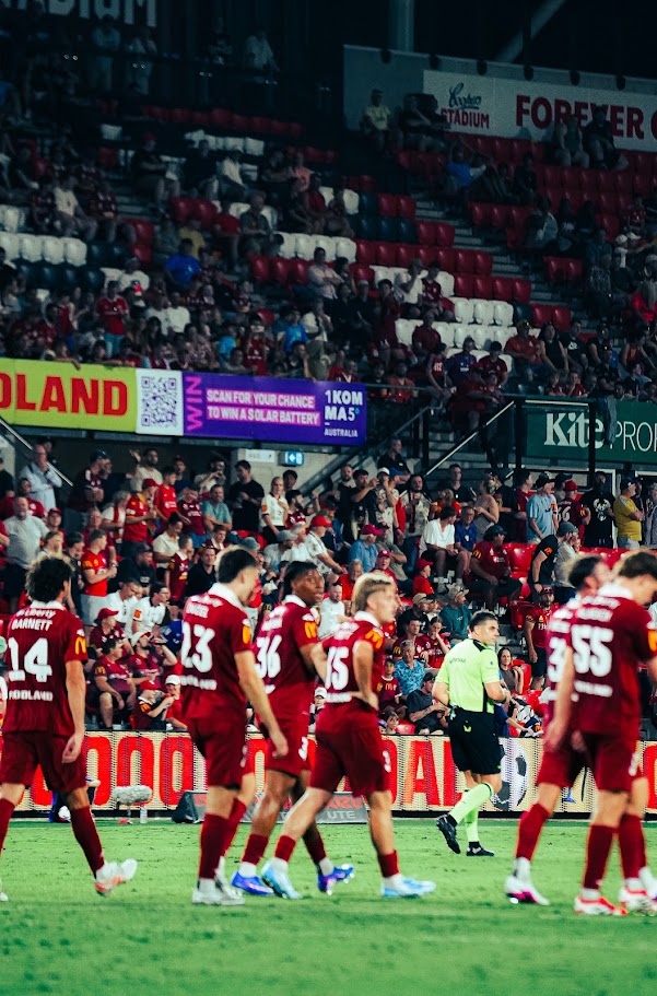 Adelaide United players and the match official walking onto the pitch at Coopers Stadium under the lights